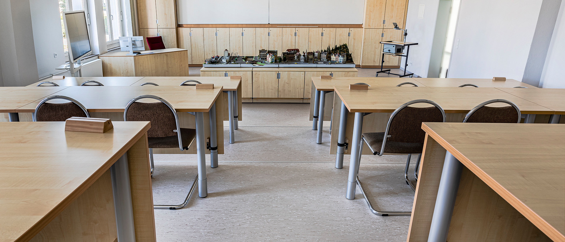 Ein leerer Hörsaal mit holzverkleideten Stühlen und Tischen.